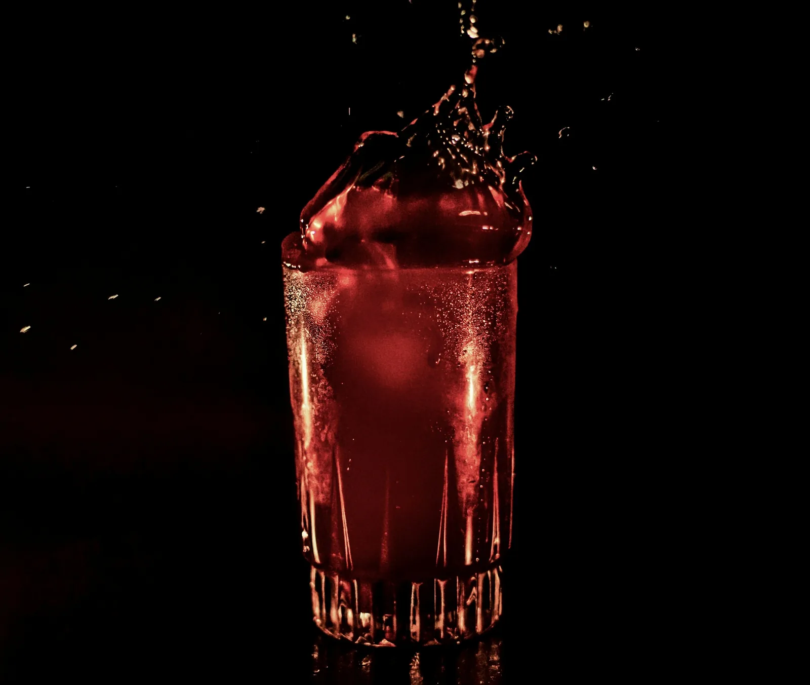 A deep red drink being poured over ice