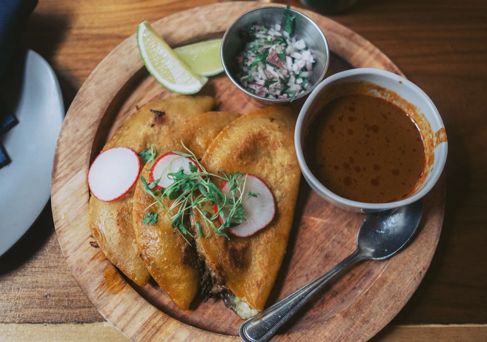 A crisp birria taco being dipped into a cup of consomé