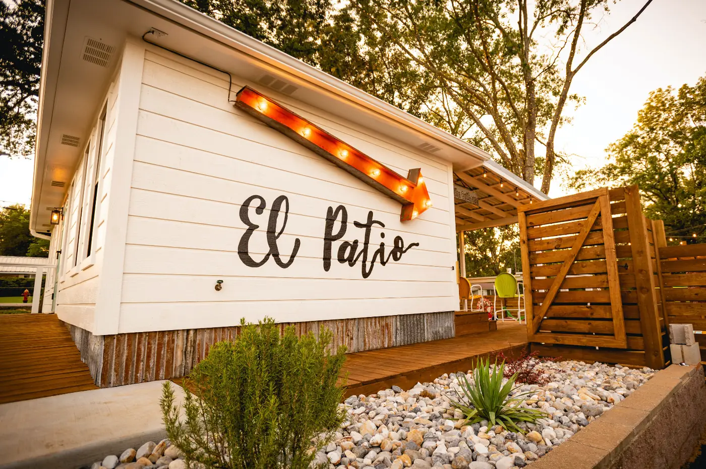 El Patio at Doc's Taco Shop - a white clapboard building with hand-lettered El Patio signage, a marquee light and a wooden pergola over the deck