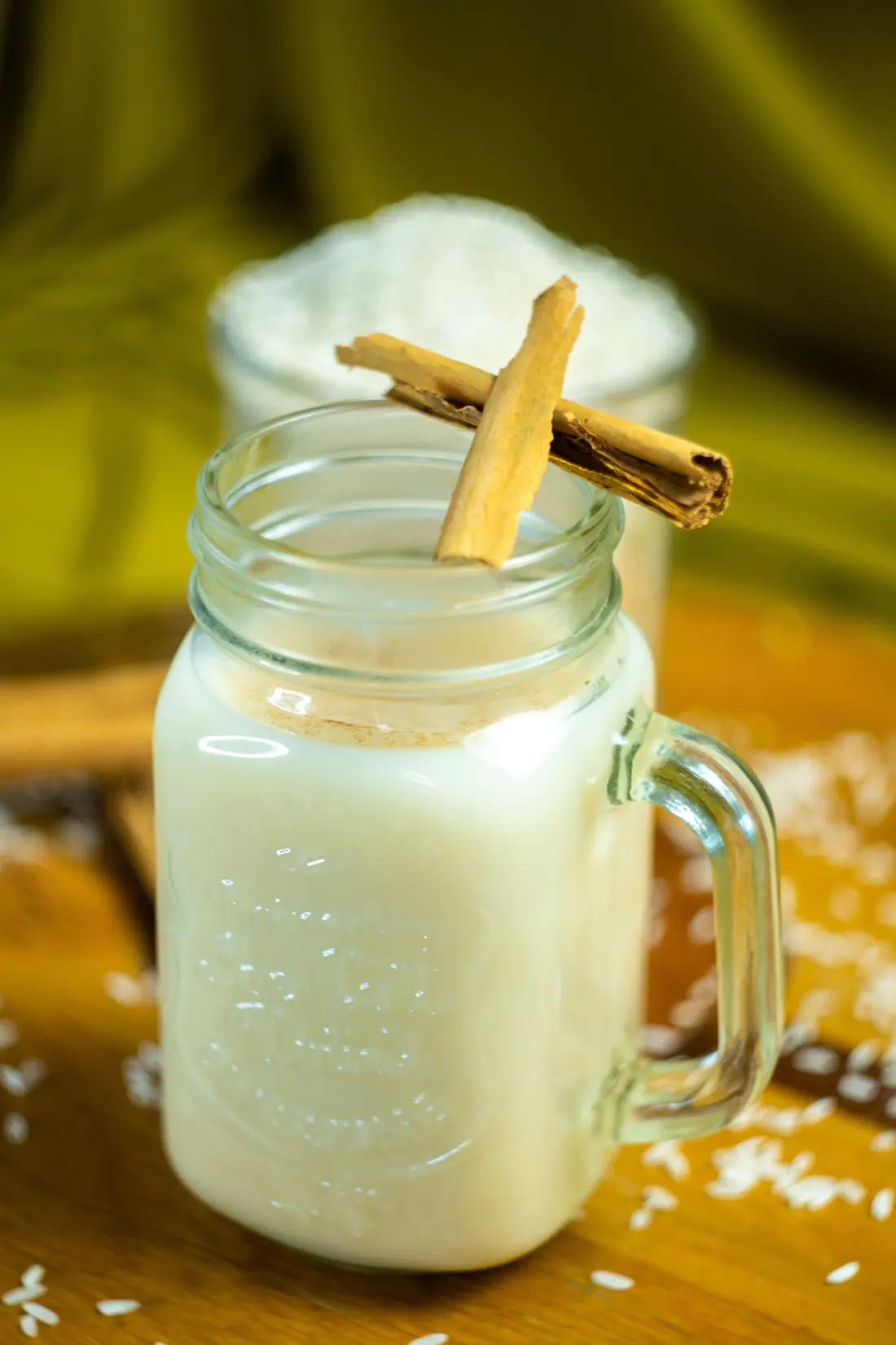 A glass jar of horchata with a cinnamon stick resting on the rim