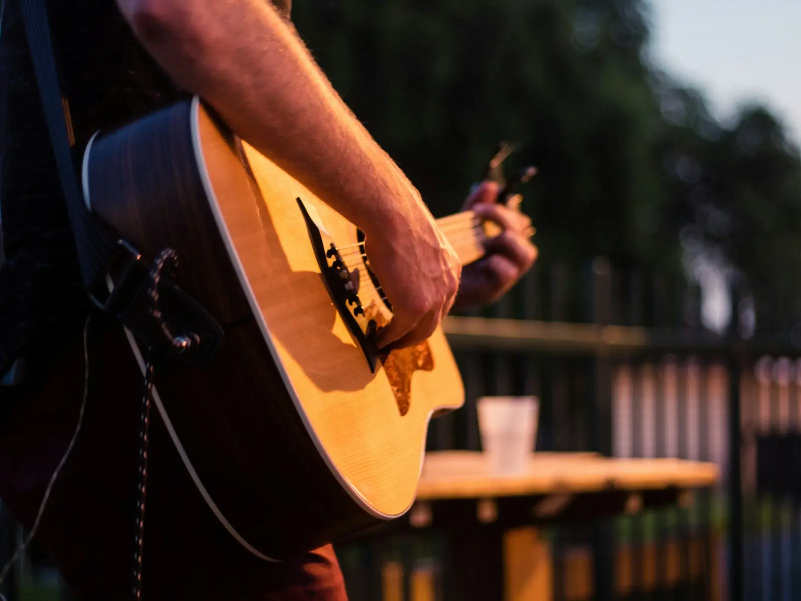 A guitarist playing outdoors at golden hour beside a picnic table