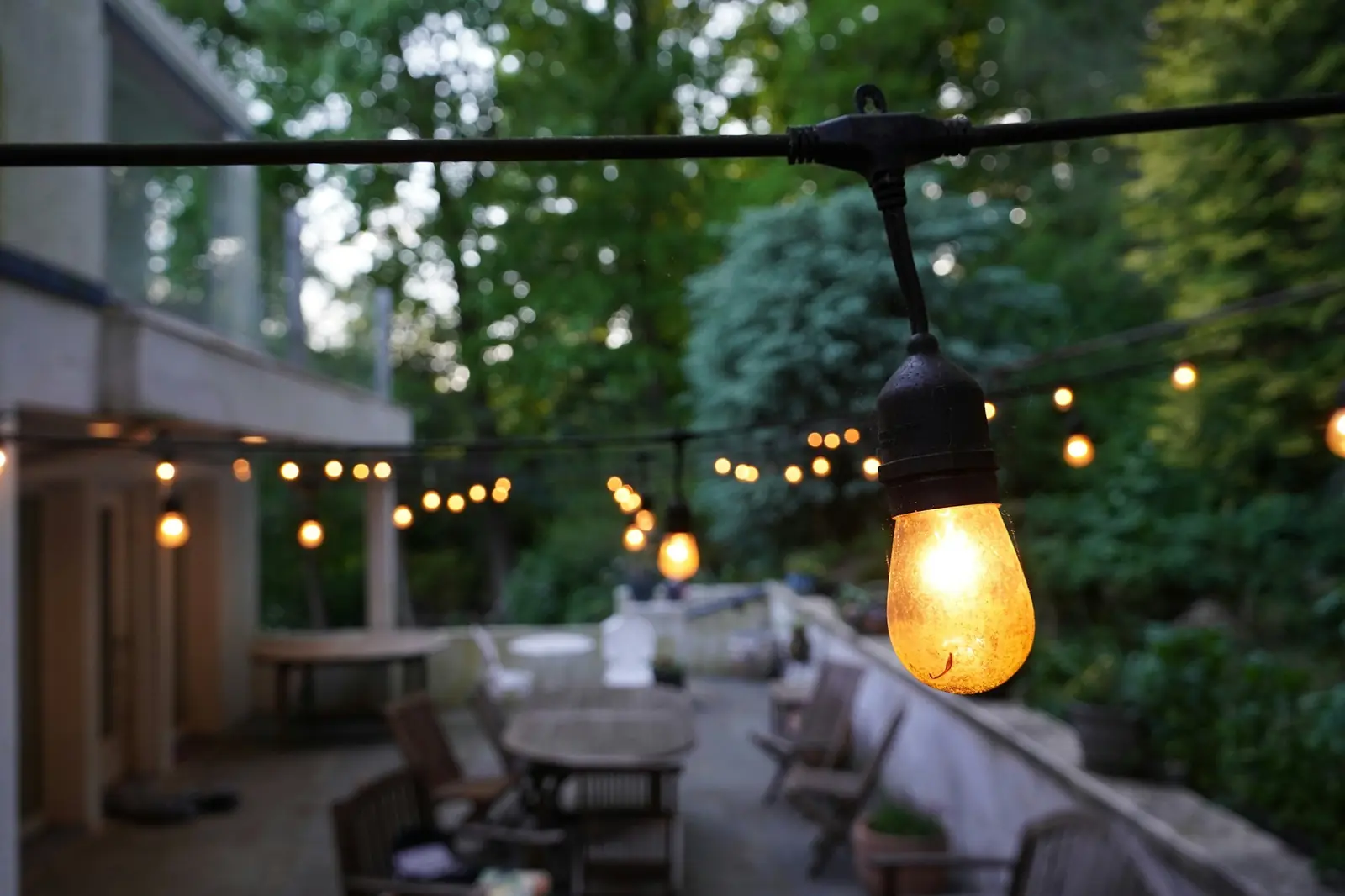 String lights glowing over an outdoor patio with tables and chairs at dusk