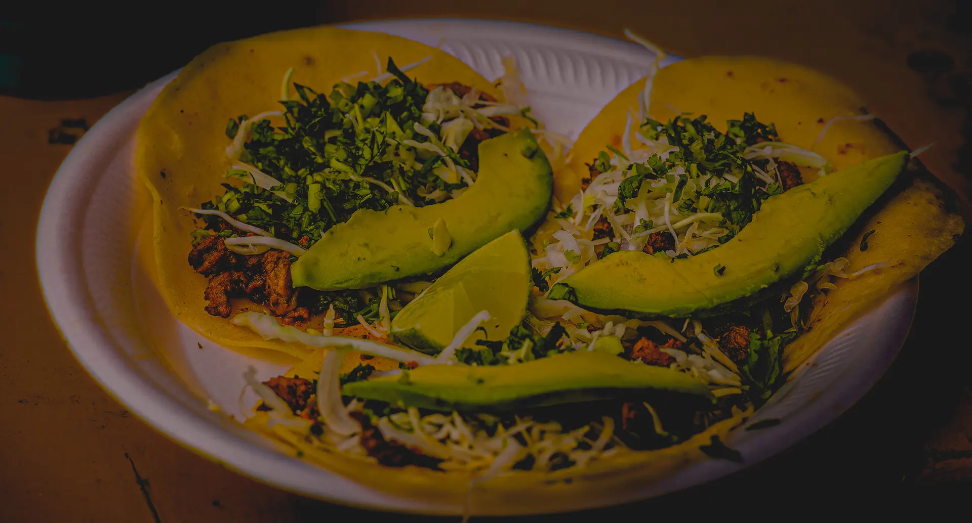 Two Doc's Taco Shop tacos on a paper plate topped with cabbage, cilantro and sliced avocado