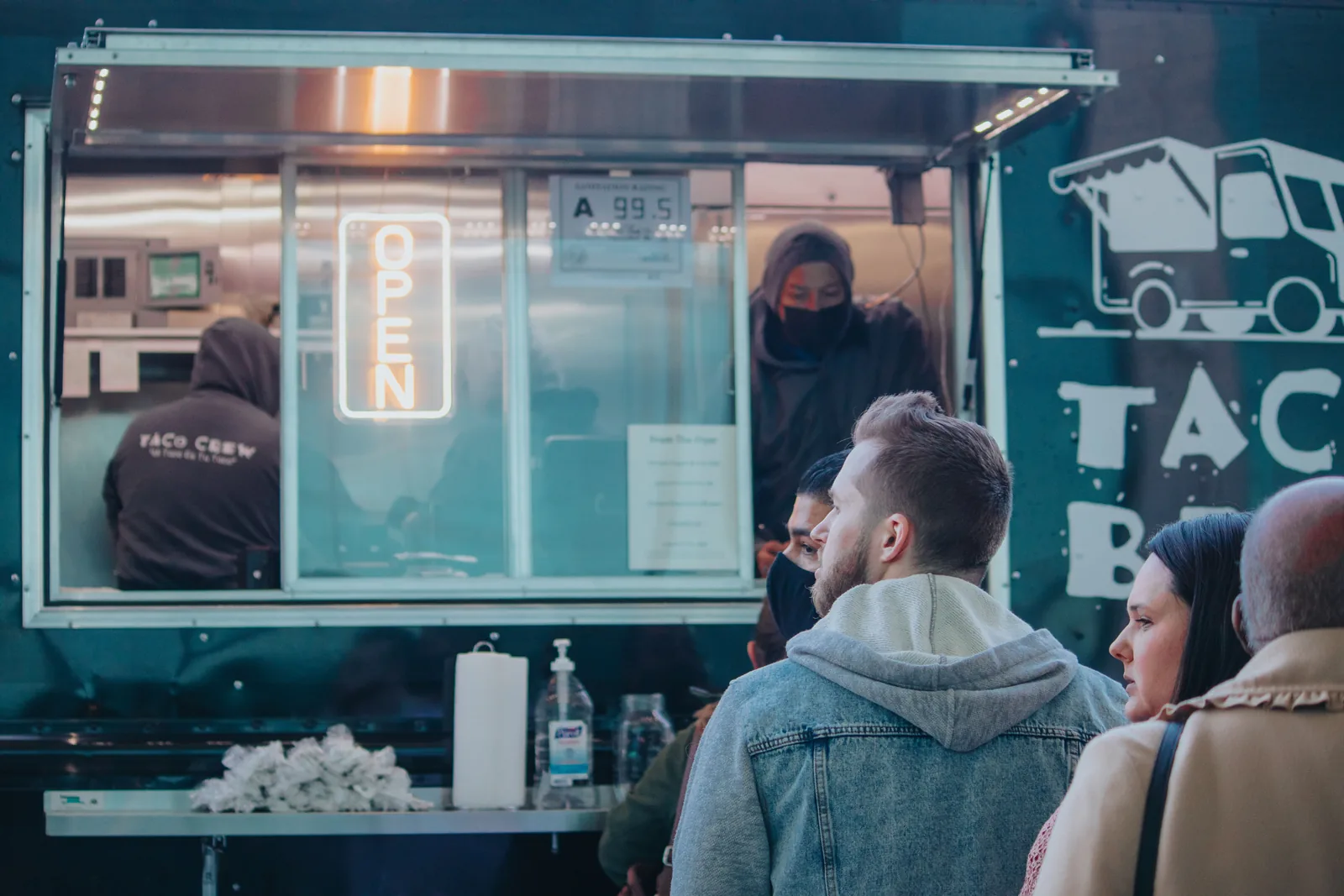 A taco truck window with customers waiting to order