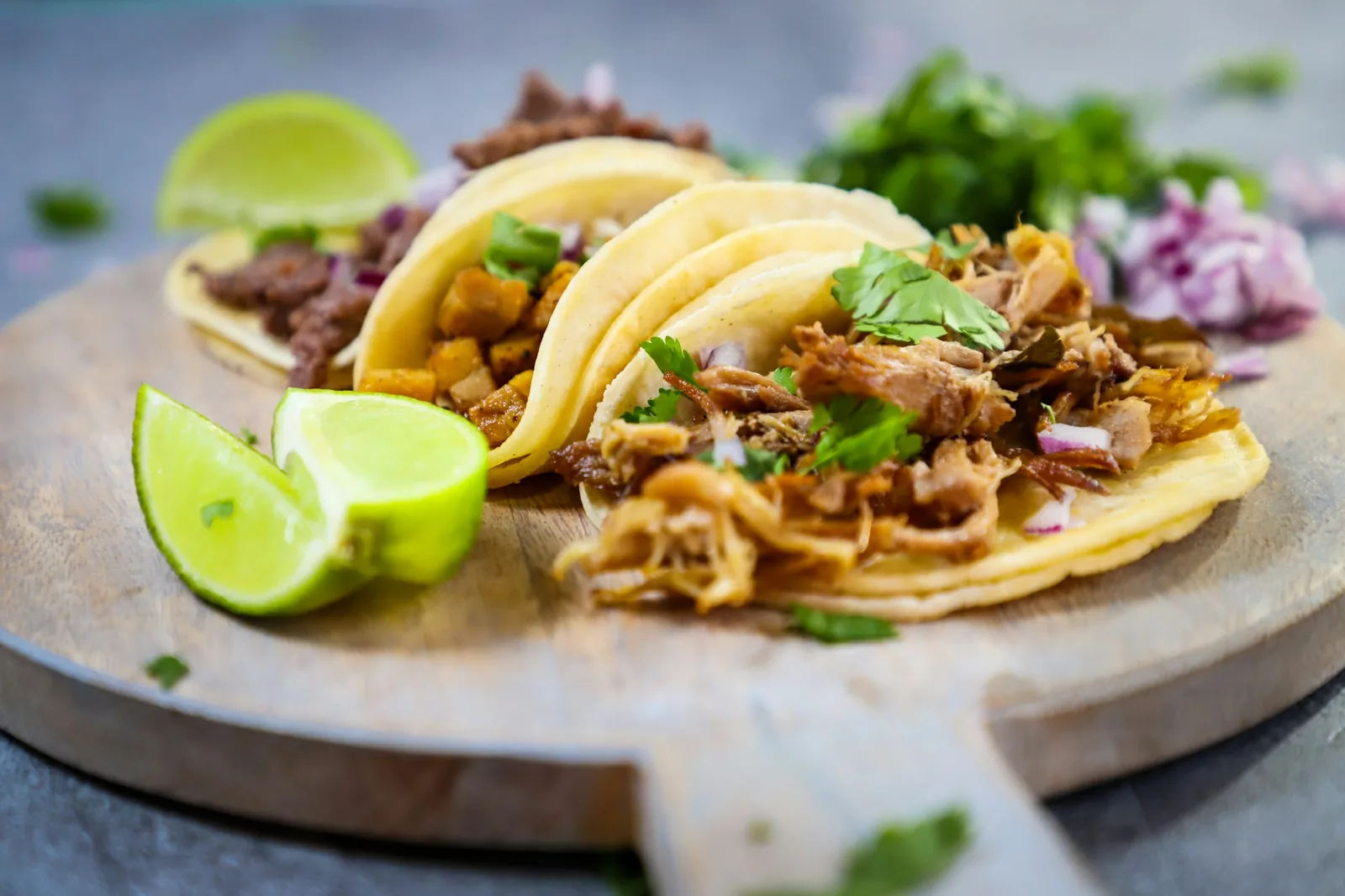 Small corn-tortilla tacos arranged on a wooden serving board